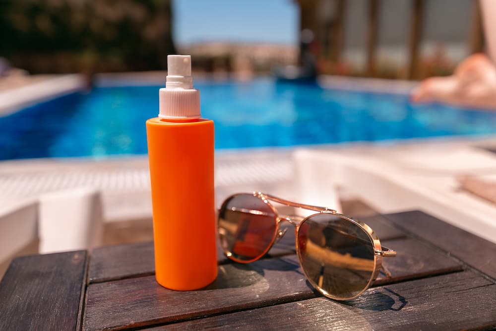 a close up image of sunglasses and a spray bottle with a background of a pool
